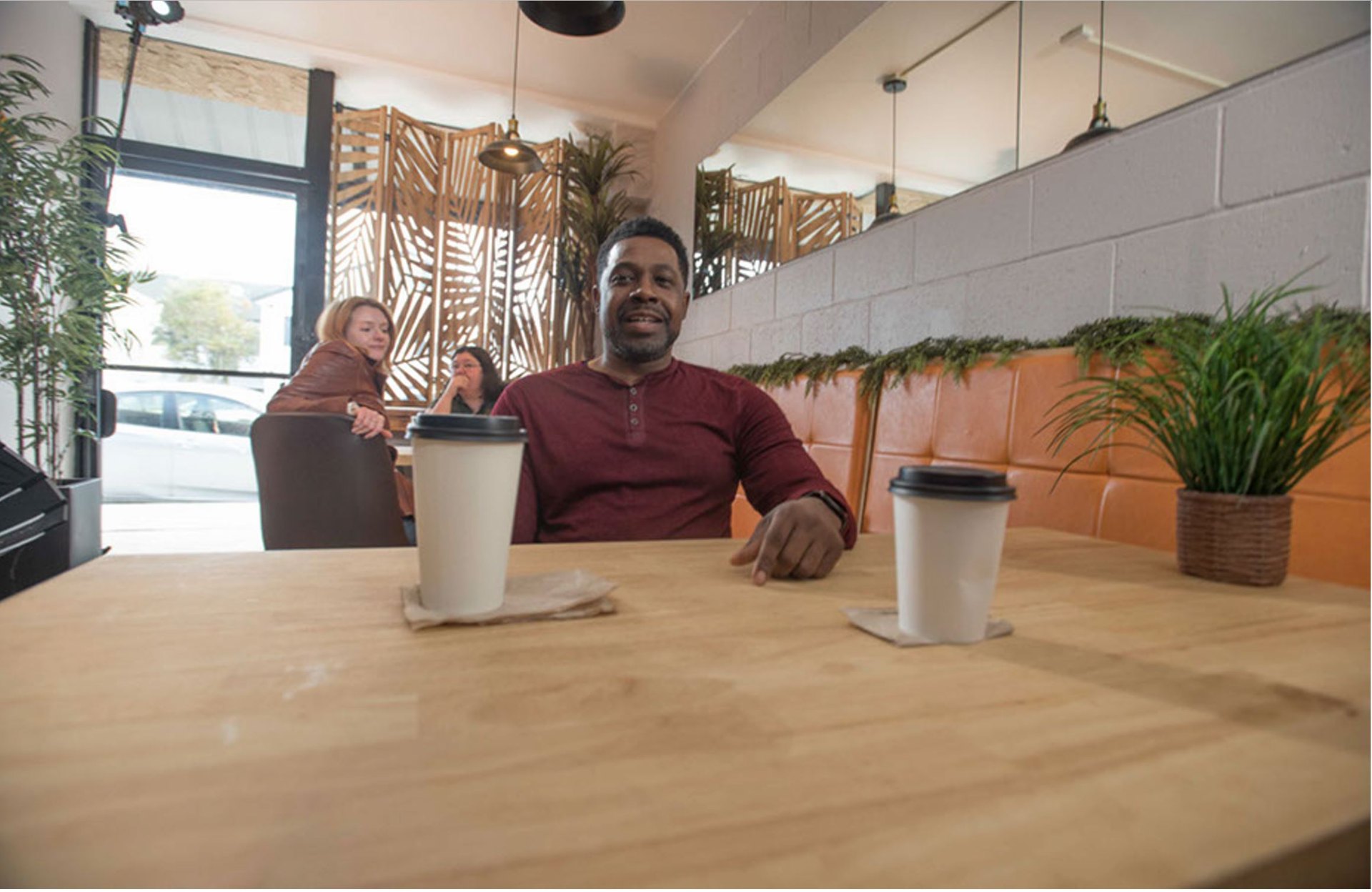 Sammy seated across two coffee cups in a sunlit cafe.