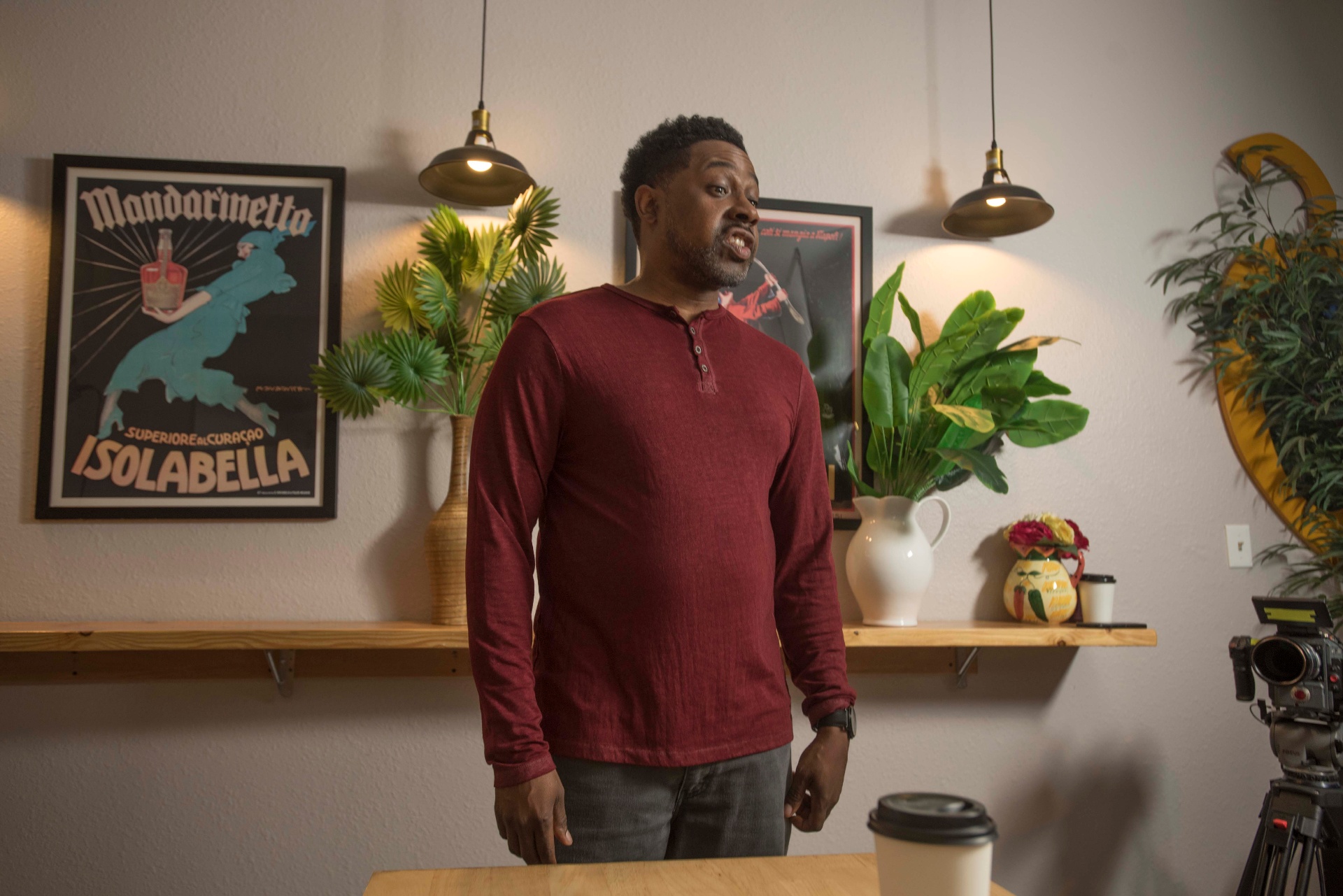 Actor mid-monologue on set, framed between pendant lights.