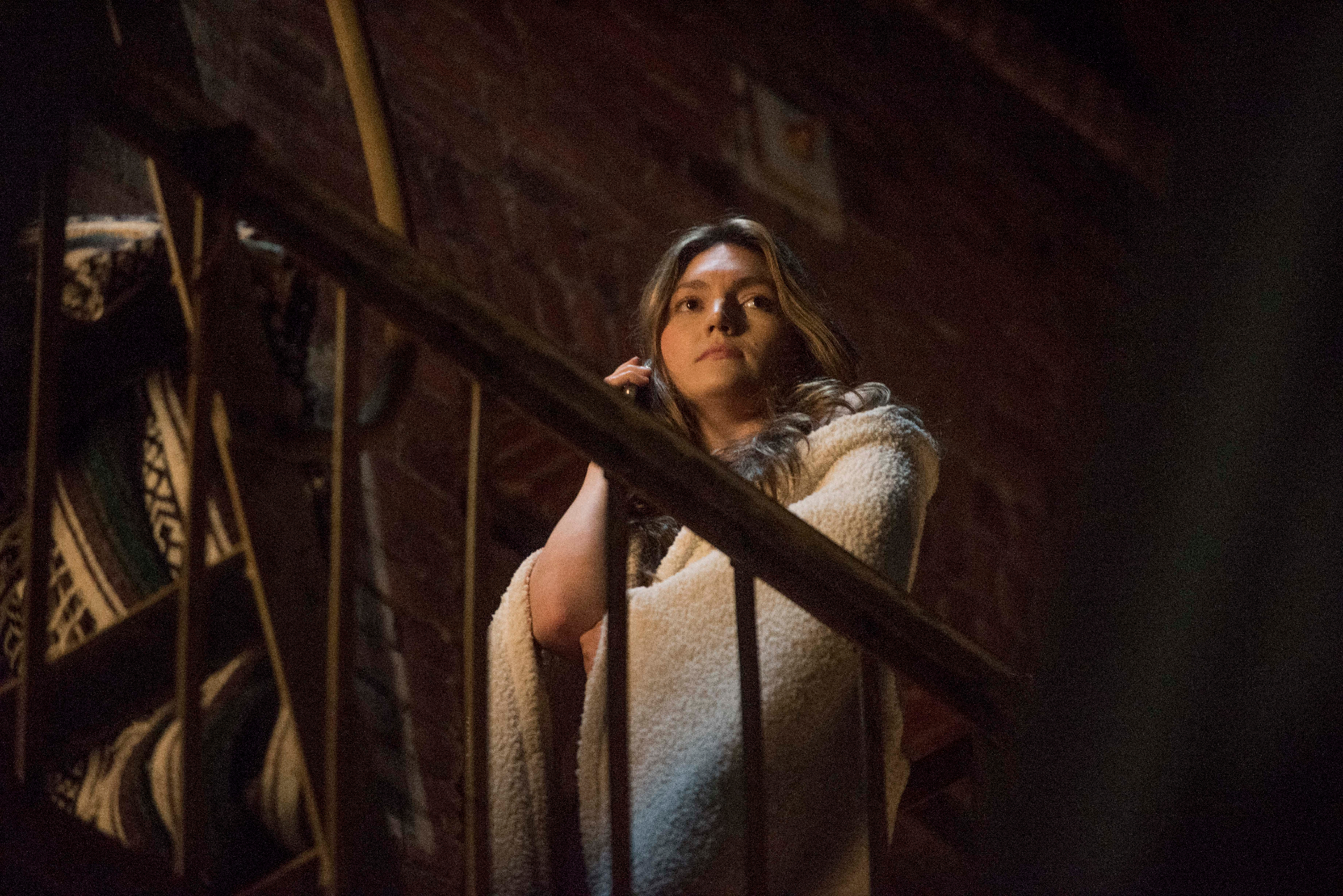 A woman wrapped in a sherpa coat stands on a fire escape at night.